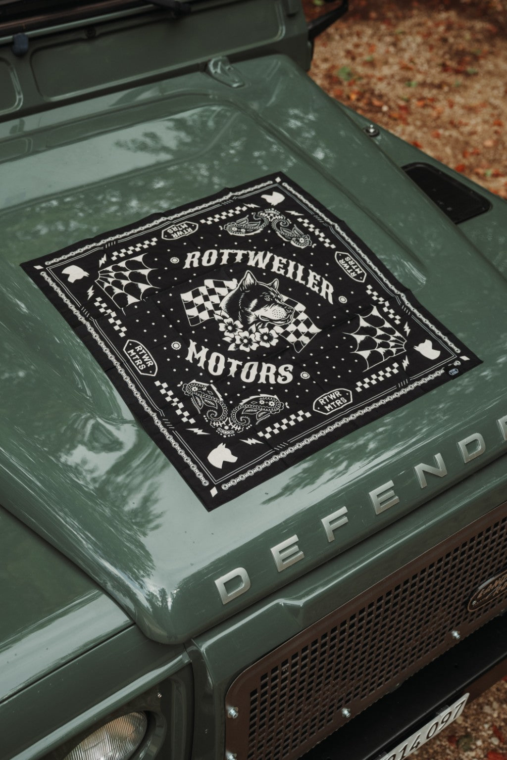 Close-up of the black Rottweiler Motors bandana with dog, racing flag and paisley artwork on a green Defender.