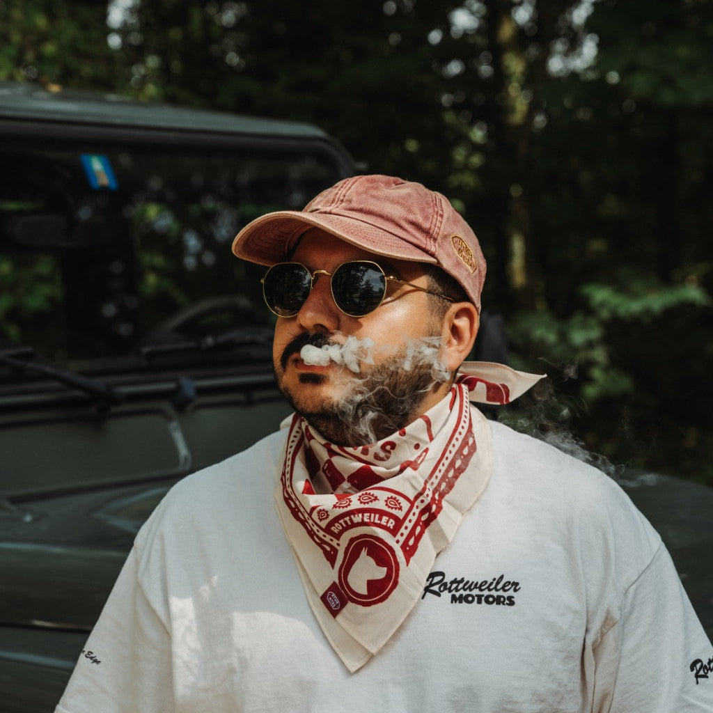 Rider wearing the red and white Rottweiler Motors bandana beside a green Defender with smoke drifting across the portrait.