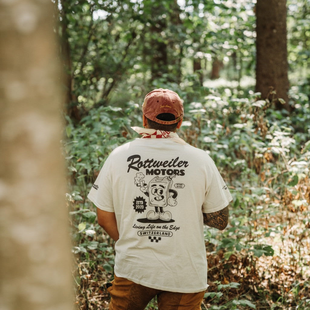 Back view of a rider wearing a white Rottweiler Motors graphic T-shirt and red-white bandana in the forest.