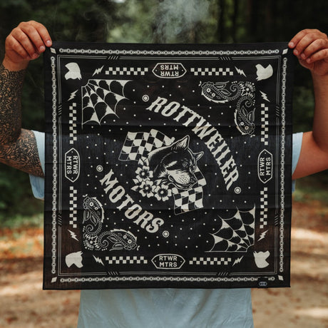 Rider holding the black Rottweiler Motors bandana with smoke drifting through a forest backdrop.