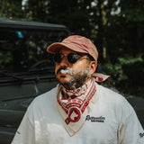 Rider wearing the red and white Rottweiler Motors bandana beside a green Defender with smoke drifting across the portrait.